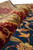 Macro of dense wool pile showing burgundy border scrollwork and the depth of the navy field