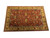 Oversize handmade Agra rug shown at an angle, rust field framed by golden saffron floral borders