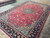 Angled view of hand-knotted wool rug showing teal spandrels, cream guard stripe and red selvage