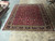 11'4" x 13'6" Persian Mashad rug photographed flat on showroom floor beside rolled inventory