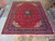 10'5" x 14' Persian Sarouk rug laid out on showroom floor beside rolled inventory rugs