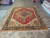 Hand-knotted Serapi design area rug displayed flat on showroom tile floor with rug stacks behind