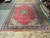 Oversize hand-knotted wool rug laid flat in warehouse showing navy border and red field