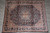 Navy blue Persian rug displayed on grey stone floor showing ivory scrolling vine main border