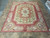 Burgundy and ivory Aubusson flat weave rug displayed on stone tile showroom floor