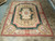 Hunter green Aubusson rug displayed on stone tile floor showing coral border and ivory corner cartouches