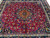 Angled floor view showing crimson red field, rust medallion and deep indigo main border of the rug