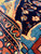 Wool pile close-up revealing hand-spun luster, midnight blue field, gold and terracotta border tones