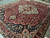 Angled view across the burgundy field, navy spandrels and palmette border of this handmade wool rug