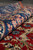 Rolled edge showing plush wool pile depth, pink rosettes on blue and red field