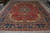 Large 11x14 Persian wool rug displayed on grey warehouse floor with ivory fringe and navy borders