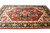 Angled floor view showing ivory spandrels, black main border and deep red hand-knotted wool pile
