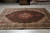 Showroom floor display of brown Tabriz wool and silk rug with ivory corner spandrels