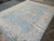 Angled floor view showing soft wool pile, ivory floral border and pale blue open field