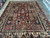 Angled showroom view of a large Persian garden rug with red, navy and cream tile panels