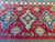 Handmade Afghan Kazak rug on floor showing deep red abrash, blue medallions and ivory rosette border