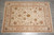 Hand-knotted wool rug on grey tile floor showing ivory field and soft rust gold border