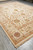 Corner perspective of large wool area rug with ivory ground and gold toned guard bands