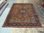 Hand-knotted Persian Tabriz rug displayed on showroom floor beside rolled Oriental rugs, brown field and navy border