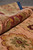 Rolled edge of the wool rug showing burgundy palmette, olive ground and thick even pile