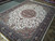 Large 10x14 hand-knotted wool rug laid across tile showroom floor, corner medallion visible