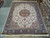9'9 x 13'9 Tabriz rug photographed flat in the warehouse beside rolled Persian rugs