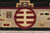 Burgundy roundel emblem and stepped ziggurat motif in the beige border of this handmade rug