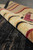 Rolled edge showing thick wool pile in cream, gold and burgundy against the black field