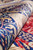 Rolled edge showing lustrous silk pile sheen, cobalt blue border and deep red field flowers