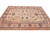 Light green Oushak rug photographed from the side, peach border rosettes and blue guard bands visible