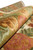 Rolled rug detail showing plush wool pile depth in olive, rose, gold and soft coral tones