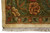 Corner detail of the olive green border with rust and ivory flower heads above cotton fringe