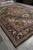 11x14 hand-knotted Serapi rug displayed on grey floor in rug warehouse with stacked inventory