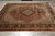 Rust and ivory hand-knotted wool and silk rug displayed flat on grey tile showroom floor