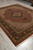 8'1" x 10' Indian hand-knotted rug shown at an angle with fringe and black floral border