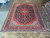 9'8" x 13'3" Persian Kashan rug displayed full length on warehouse floor beside rolled rugs