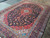 Angled view showing glossy wool pile, turquoise guard borders and the red central medallion