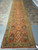 Extra long hand-knotted runner displayed on showroom floor, terracotta rose field and repeating palmette rosettes