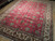 Large red Tabriz rug shown at an angle on hardwood, soft storage fold lines visible