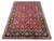 Hand-knotted Indian area rug displayed at an angle showing red field, black border and sage guard stripes