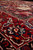 Low angle across deep red main border highlighting ivory vines, navy palmettes and dense wool pile