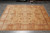 Neutral gold Ziegler area rug laid on grey tile floor showing soft green and rust tones