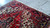 Hand-knotted wool pile photographed on a concrete floor, showing ivory corners, red field and fringe