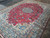 Angled view showing deep red field, sage green border florals and dense wool pile