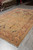 Coral and camel Oriental rug in showroom with rolled rugs stacked behind it