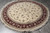 Round Oriental rug photographed at an angle on grey tile, ivory field and deep red border