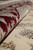 Folded edge revealing dense wool and silk pile depth along the crimson floral border