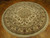 Angled floor view of the cream round rug, dense floral field and sage green main border