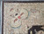 Corner close-up with beige spandrel bracket, small red rosette, brown selvedge and clean ivory fringe