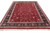 Hand-knotted wool and silk area rug angled on white, showing crimson field and navy floral border